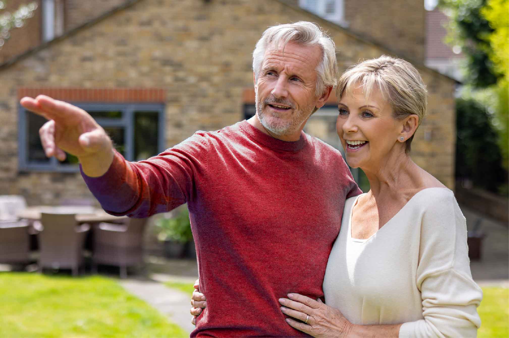 A couple in their 60s outside a house, looking into the distance.