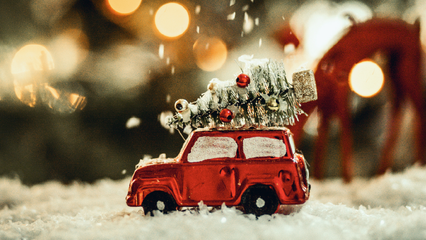 A red toy car with a Christmas tree on the roof, with a snowy background.