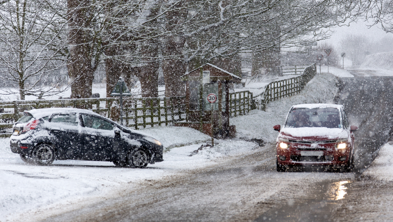 Two cars on a snowy road. One has skidded off onto a grass verge.