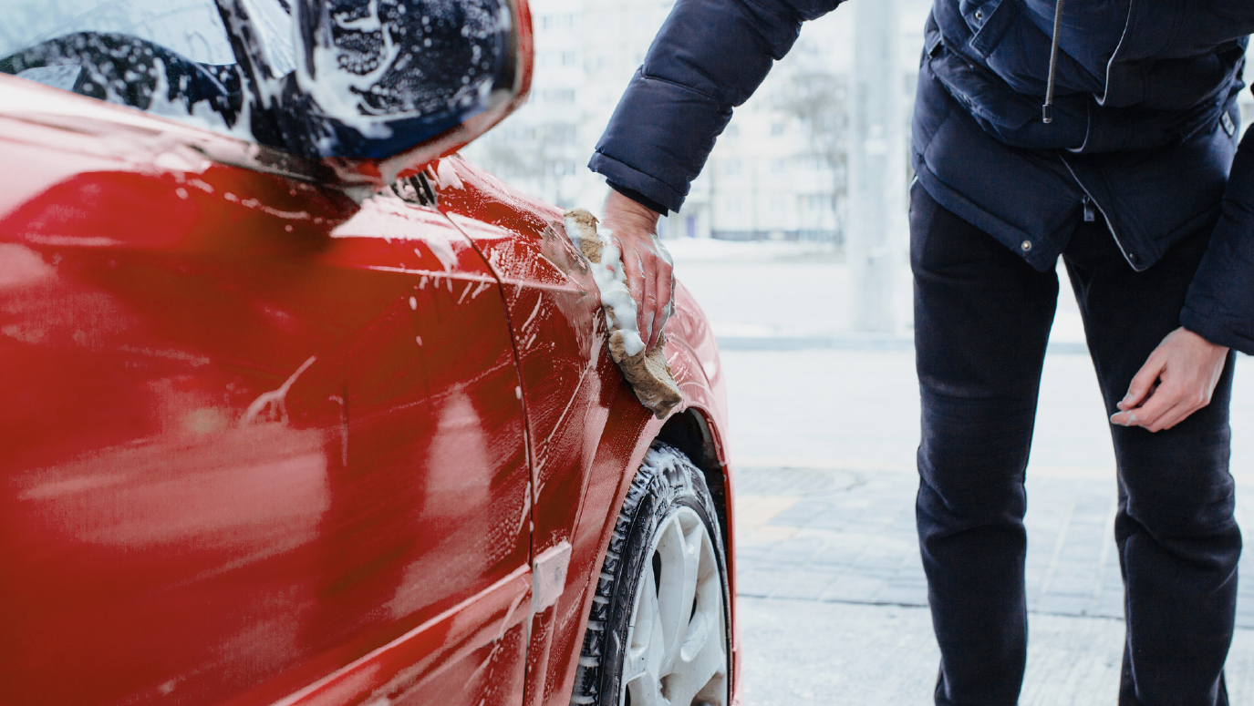 A man standing outside in winter, washing a red car by hand.