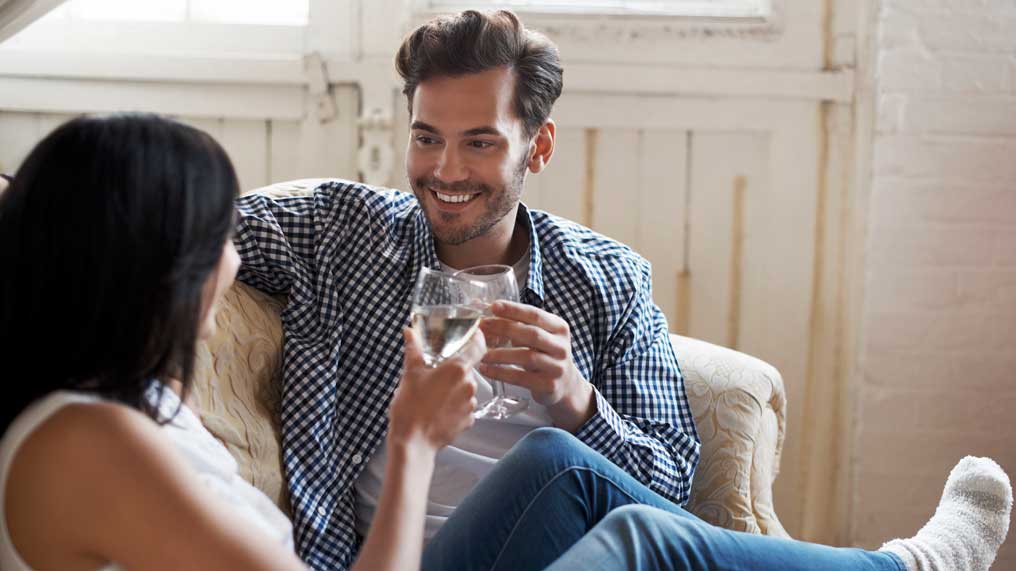 A couple share a drink on their sofa.