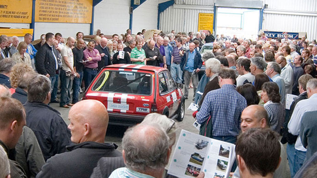 a crowd of people surround a car at auction