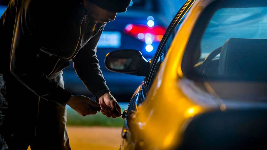 A thief attempts to break into a car.