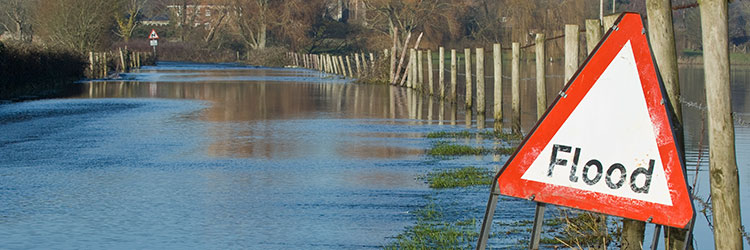 Red and white flood sign next to flooded road